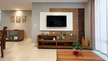Uma sala de estar moderna com televisão de tela plana na parede, móveis de madeira e uma área de jantar ao fundo.