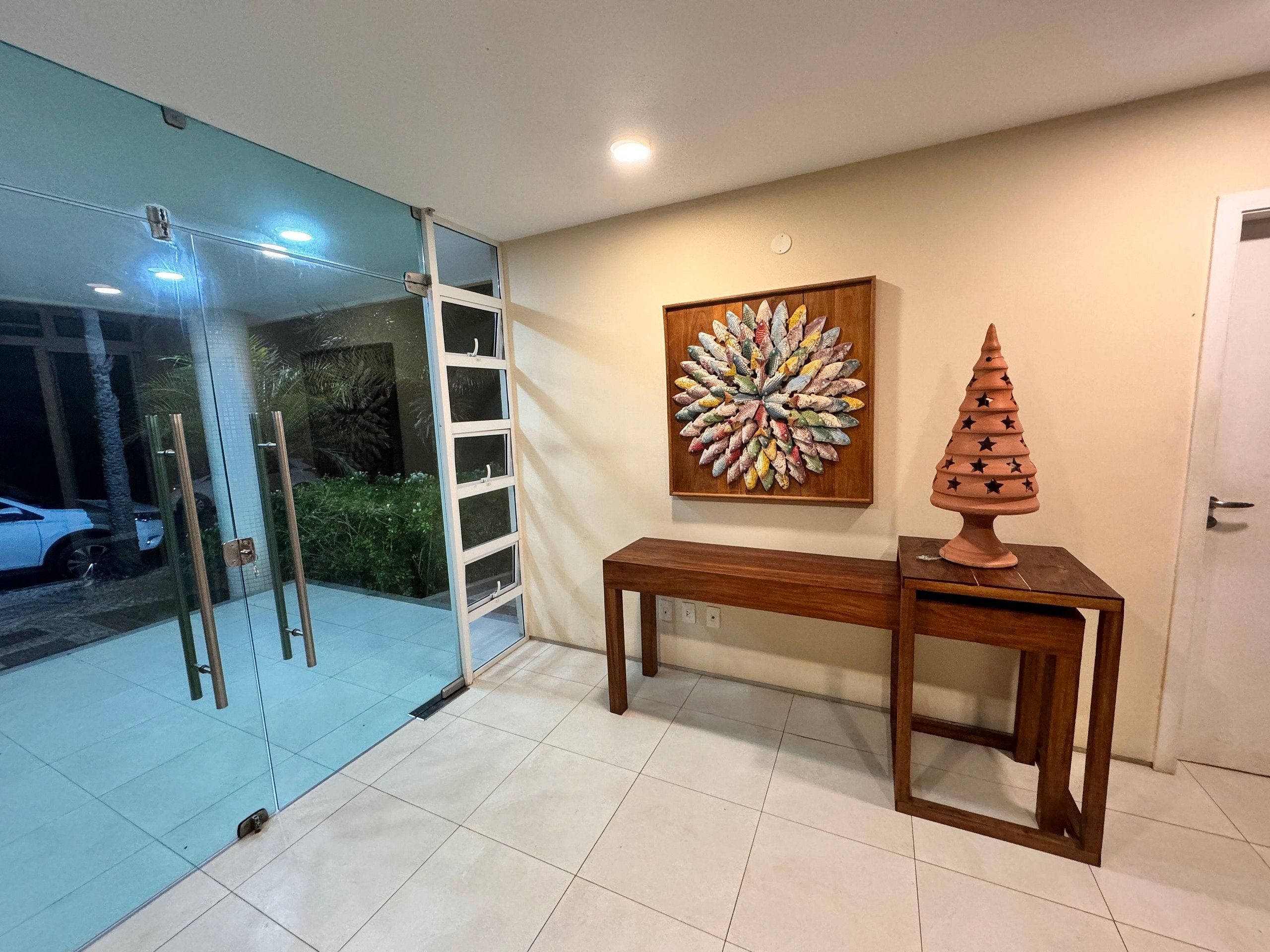 A room with a glass door, a wooden bench, a decorative wall piece, and a small tree sculpture.