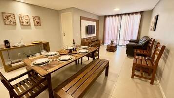 A dining area with a wooden table set for four, a sofa, and a TV mounted on the wall.