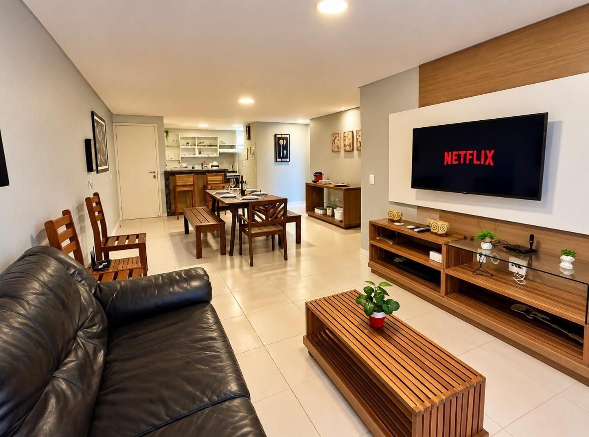 Uma sala de estar moderna com sofá de couro, mesa de centro de madeira e TV de tela plana na parede.