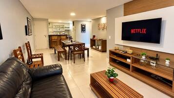 Uma sala de estar moderna com sofá de couro, mesa de centro de madeira e TV de tela plana na parede.