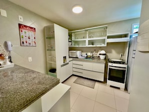 A kitchen with a granite countertop, white cabinets, a microwave, a stove, and a glass display cabinet.