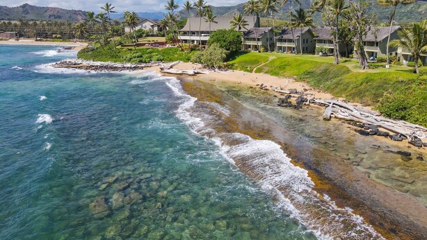 A coastal resort with clear waters, a sandy beach, and a backdrop of mountains and palm trees. - Kauai Hale Awapuhi By Coldwell Banker Island Vacations (Kapaa)