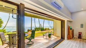 A modern room with a sliding glass door leading to a patio with outdoor furniture and a view of the ocean. - Kauai Hale Awapuhi By Coldwell Banker Island Vacations (Kapaa)