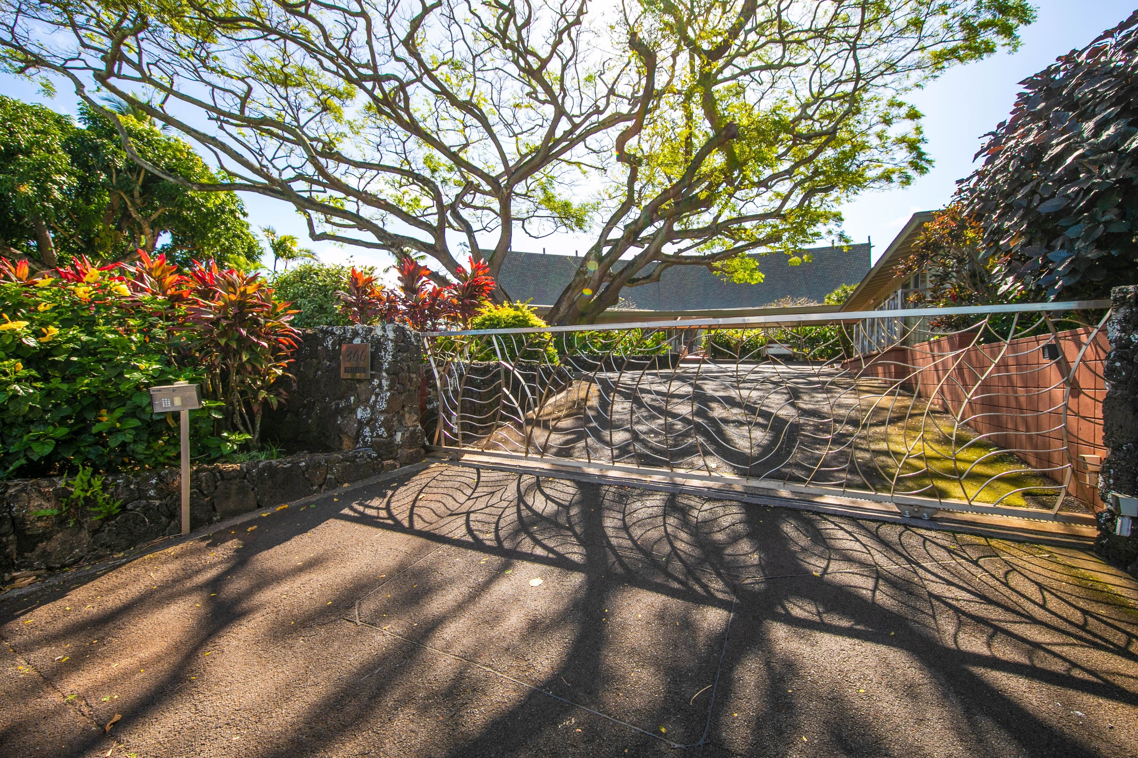A gated entrance with a metal fence, surrounded by lush greenery and trees.