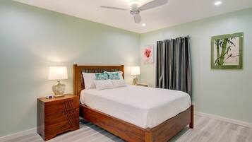 A bedroom with a wooden bed, two bedside tables with lamps, a ceiling fan, and artwork on the walls.