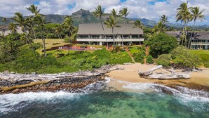 A beachfront hotel with clear waters, palm trees, and a mountainous backdrop. - Kauai Hale Awapuhi By Coldwell Banker Island Vacations (Kapaa)