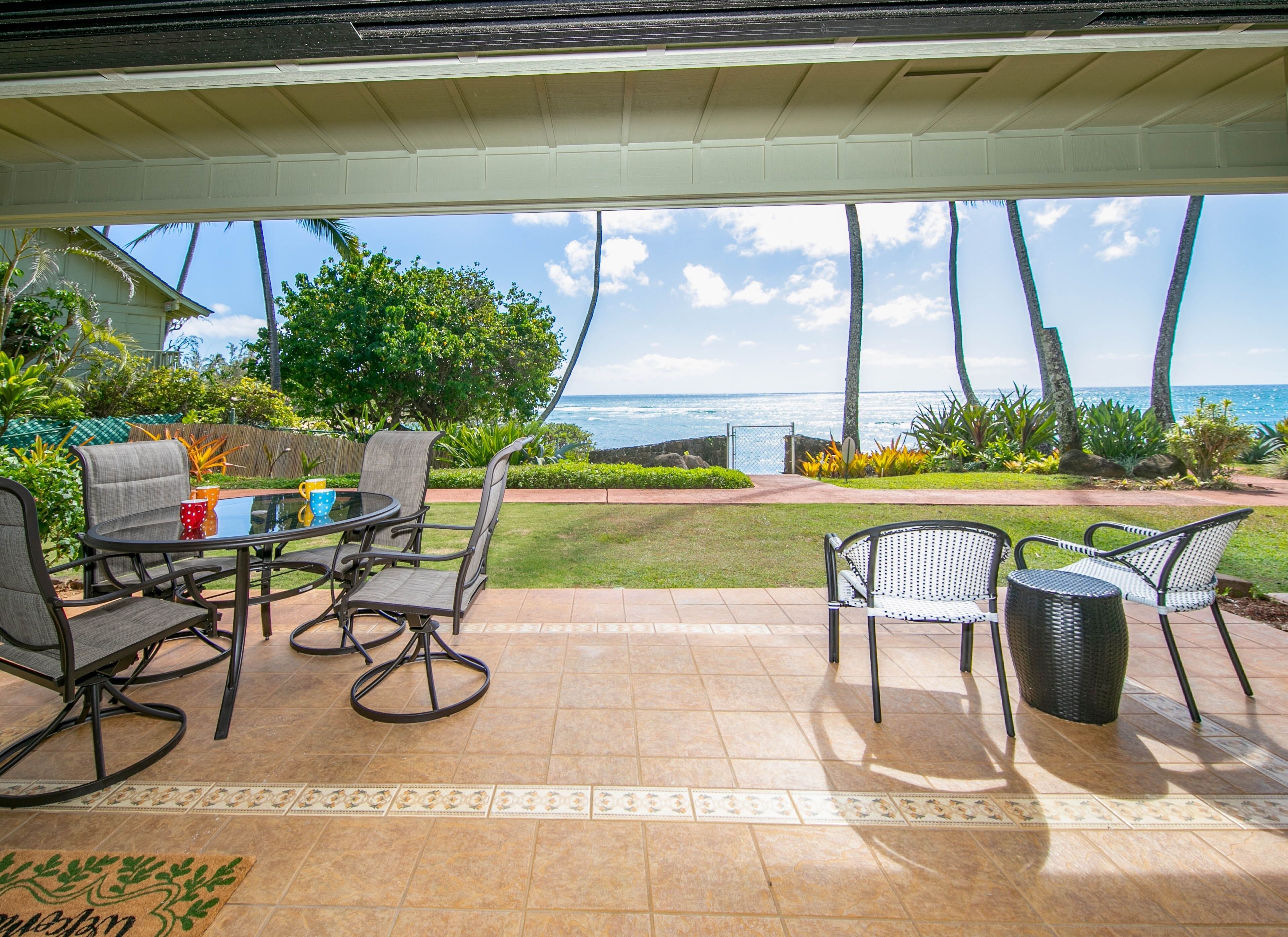 A covered patio with a view of the ocean, featuring a table and chairs, a wicker basket, and a doormat.
