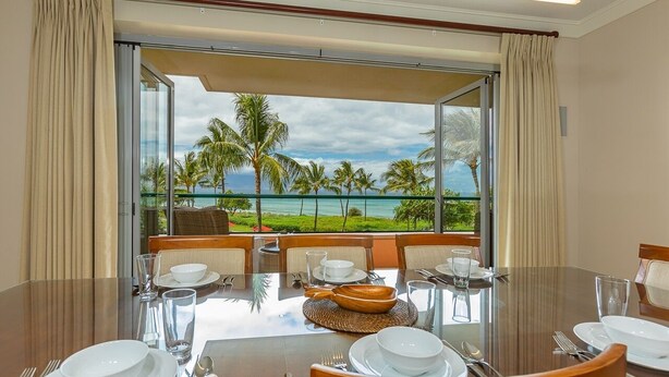 A dining area with a table set for four, overlooking a beach with palm trees and the ocean. - Honua Kai Konea by Coldwell Banker Island Vacations (Lahaina)