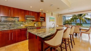 A modern kitchen with a large island, wooden cabinets, and a view of the ocean. - Honua Kai Konea by Coldwell Banker Island Vacations (Lahaina)