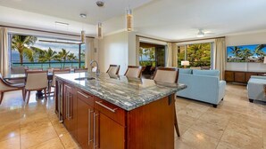A spacious living area with a large island kitchen, a sofa, and a TV. - Honua Kai Konea by Coldwell Banker Island Vacations (Lahaina)