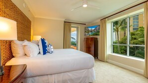 A hotel room with a large bed, a ceiling fan, a TV, and a view of palm trees through the window. - Honua Kai Konea by Coldwell Banker Island Vacations (Lahaina)