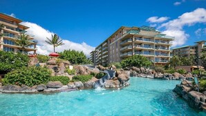 A resort pool with a water slide, surrounded by rock formations and lush greenery. - Honua Kai Konea by Coldwell Banker Island Vacations (Lahaina)