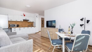 Una sala moderna con un sofá, una mesa de comedor con sillas, una zona de cocina con armarios y electrodomésticos, y un televisor de pantalla plana.