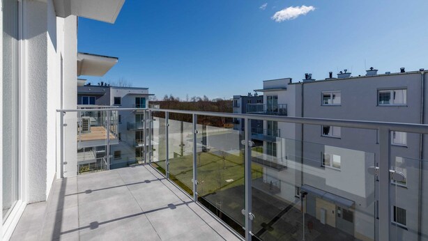 Un edificio de apartamentos moderno con balcón de vidrio, cielo despejado y vistas de edificios vecinos.