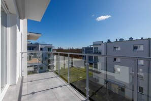 Ein modernes Mehrfamilienhaus mit Glasbalkon, blauem Himmel und Blick auf benachbarte Gebäude.