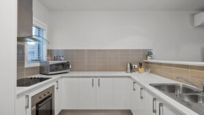 Et moderne køkken med hvide skabe, en stålvask, en mikrobølgeovn og en elkedel.