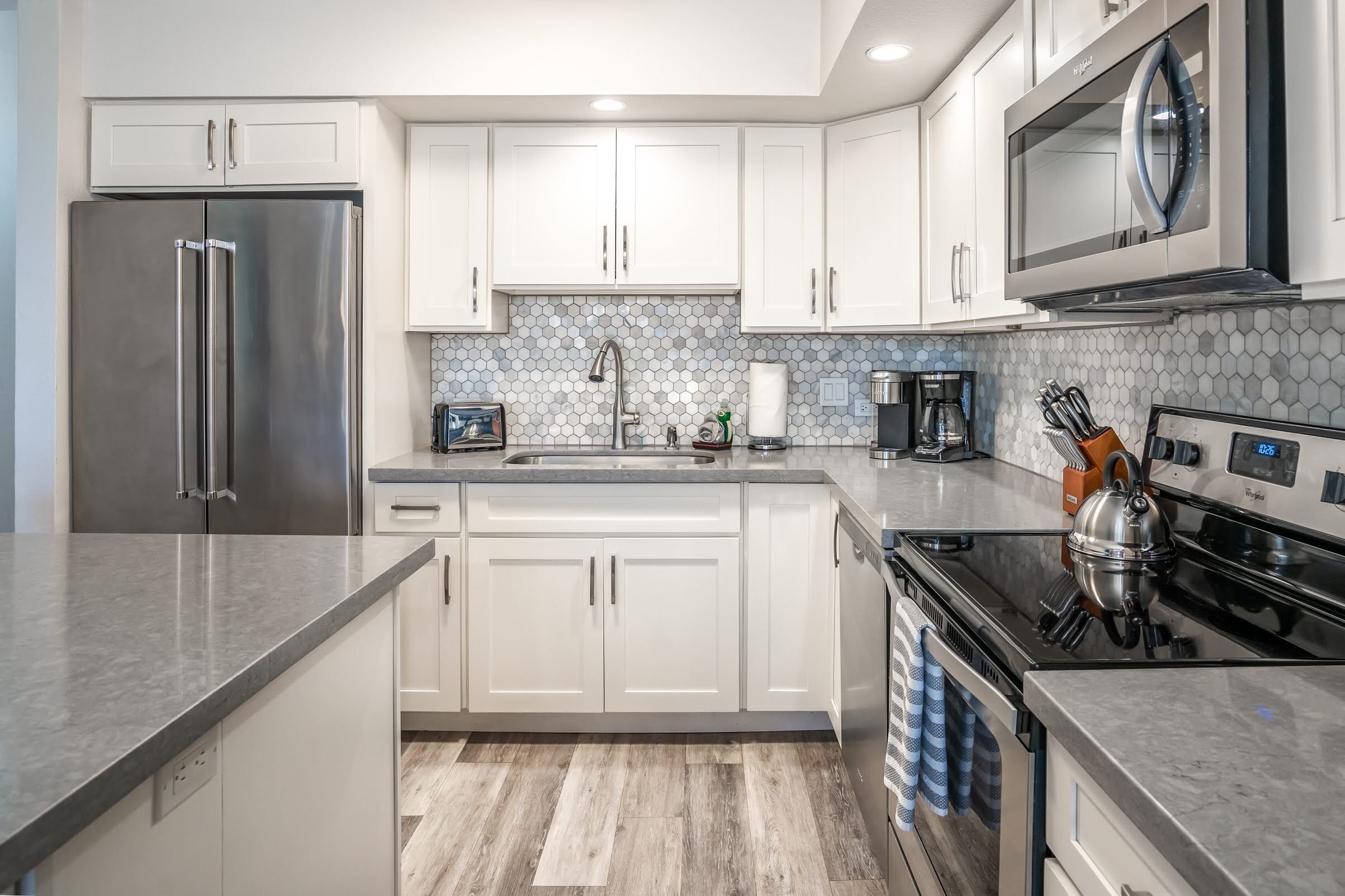 A modern kitchen with white cabinets, a stainless steel refrigerator, a microwave, and a kettle on the stove.