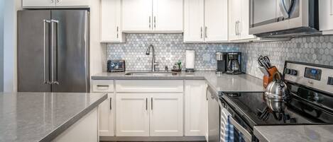 A modern kitchen with white cabinets, a stainless steel refrigerator, a microwave, and a kettle on the stove.