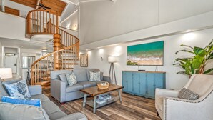 A spacious living room with a wooden spiral staircase, a grey sofa set, a coffee table, and a blue cabinet. - Kamaole Sands Two Bedrooms by Coldwell Banker Island Vacations (Kihei)