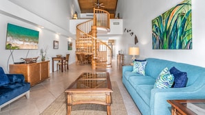 A spacious living area with a wooden spiral staircase, a blue sofa, and a large abstract painting. - Kamaole Sands Two Bedrooms by Coldwell Banker Island Vacations (Kihei)