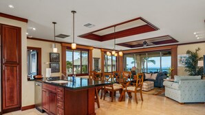 A spacious kitchen with a large island, wooden cabinets, and a dining area with chairs and a sofa. - Big Island Waiulaula at Mauna Kea by Coldwell Banker Island Vacations (Kamuela)