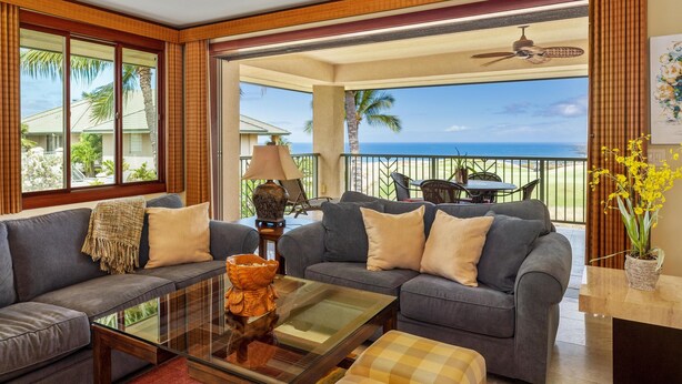 A spacious living room with a large gray sofa, a glass coffee table, and a view of the ocean through large windows. - Big Island Waiulaula at Mauna Kea by Coldwell Banker Island Vacations (Kamuela)