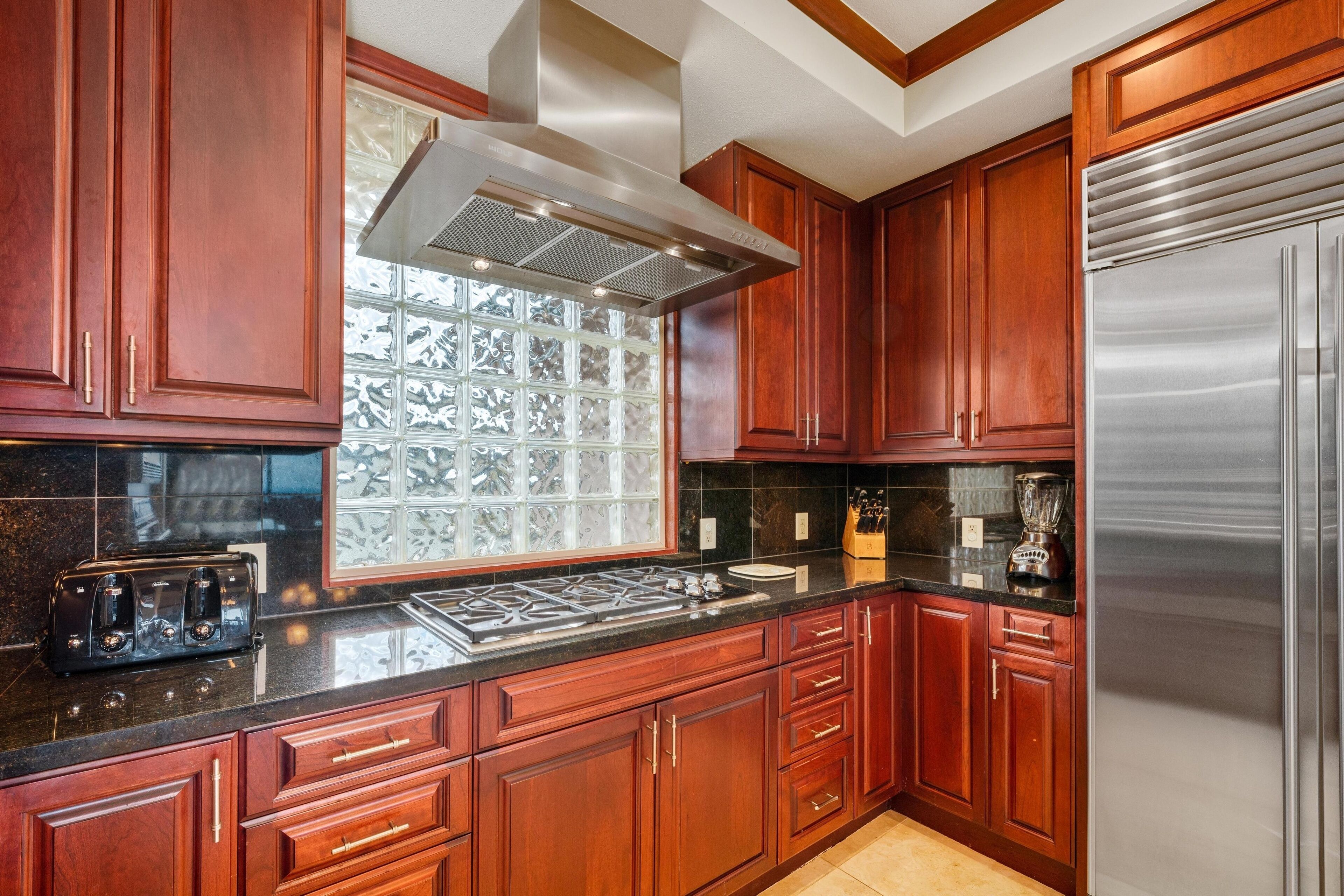 A kitchen with wooden cabinets, a stainless steel refrigerator, a gas stove, and a window with decorative glass.