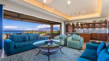 A spacious living area with a large sofa, a glass coffee table, and a view of the ocean.