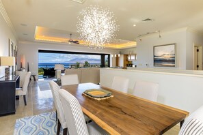 A modern dining area with a wooden table, striped chairs, and a view of the ocean. - Ho'olei Ocean View by Coldwell Banker Island Vacations (Kihei)