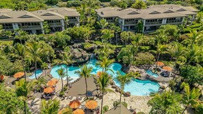 Un resort con varias edificaciones, un área de piscina central con palmeras y una cascada.