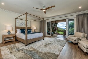 Una cama con dosel, un ventilador de techo, un ventanal con cortinas y vistas al exterior.