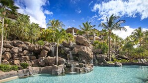 Ein Resort-Pool mit klarem Wasser, umgeben von Palmen und einem Felswasserfall.