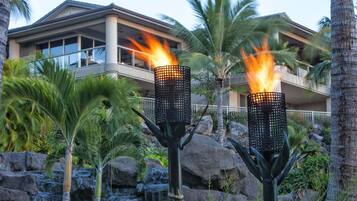 A modern hotel with a pool area, featuring two lit torches and a waterfall.