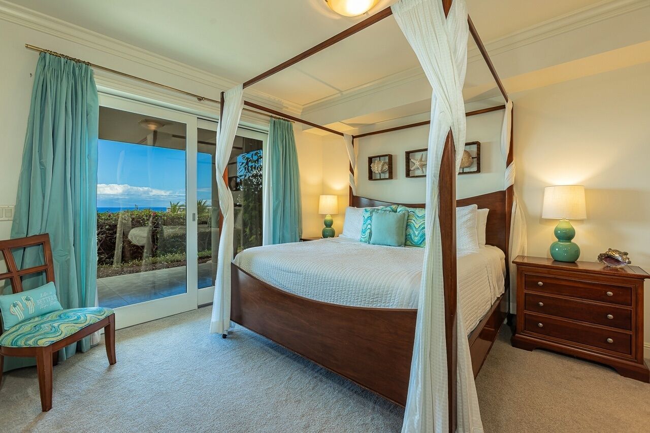 A bedroom with a four-poster bed, a chair, a nightstand, and a view of the outdoors.