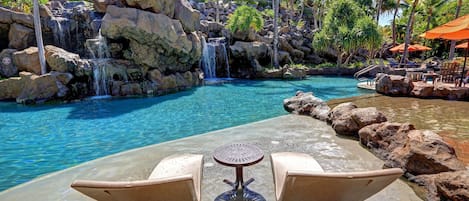 A poolside area with a waterfall, lounge chairs, and a view of a resort building.