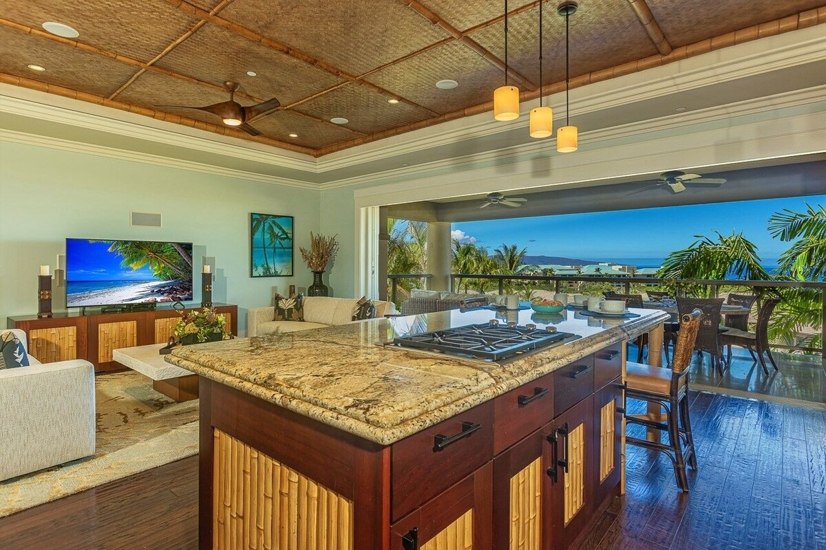 A spacious kitchen with a large island, a dining area with outdoor seating, and a view of the ocean.