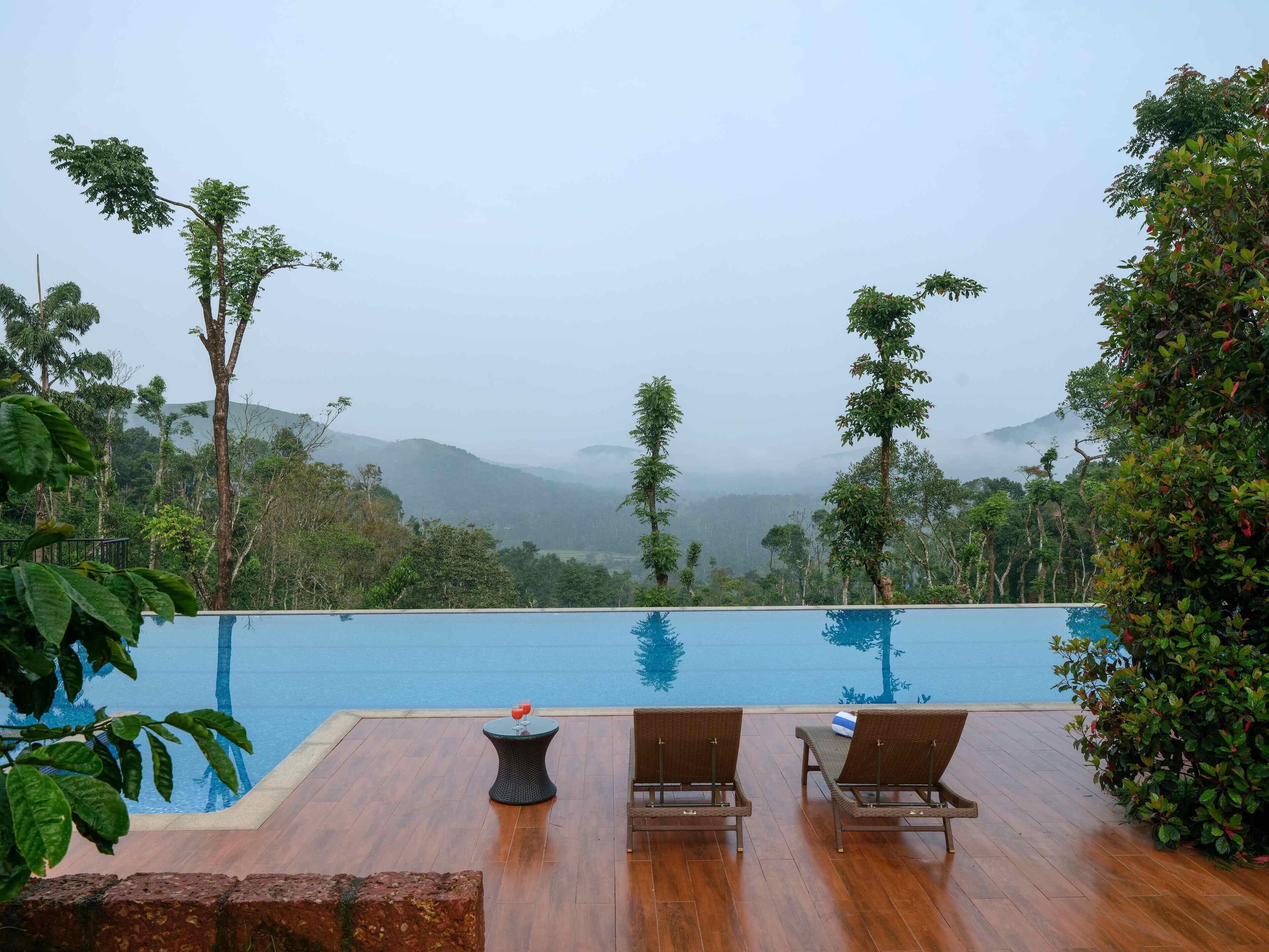 A poolside area with lounge chairs and a table, surrounded by lush greenery and overlooking a mountainous landscape.