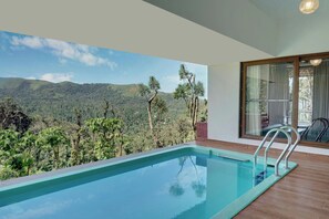 Piscina con vistas a la montaña, una terraza de madera y un ventanal que da a un balcón.