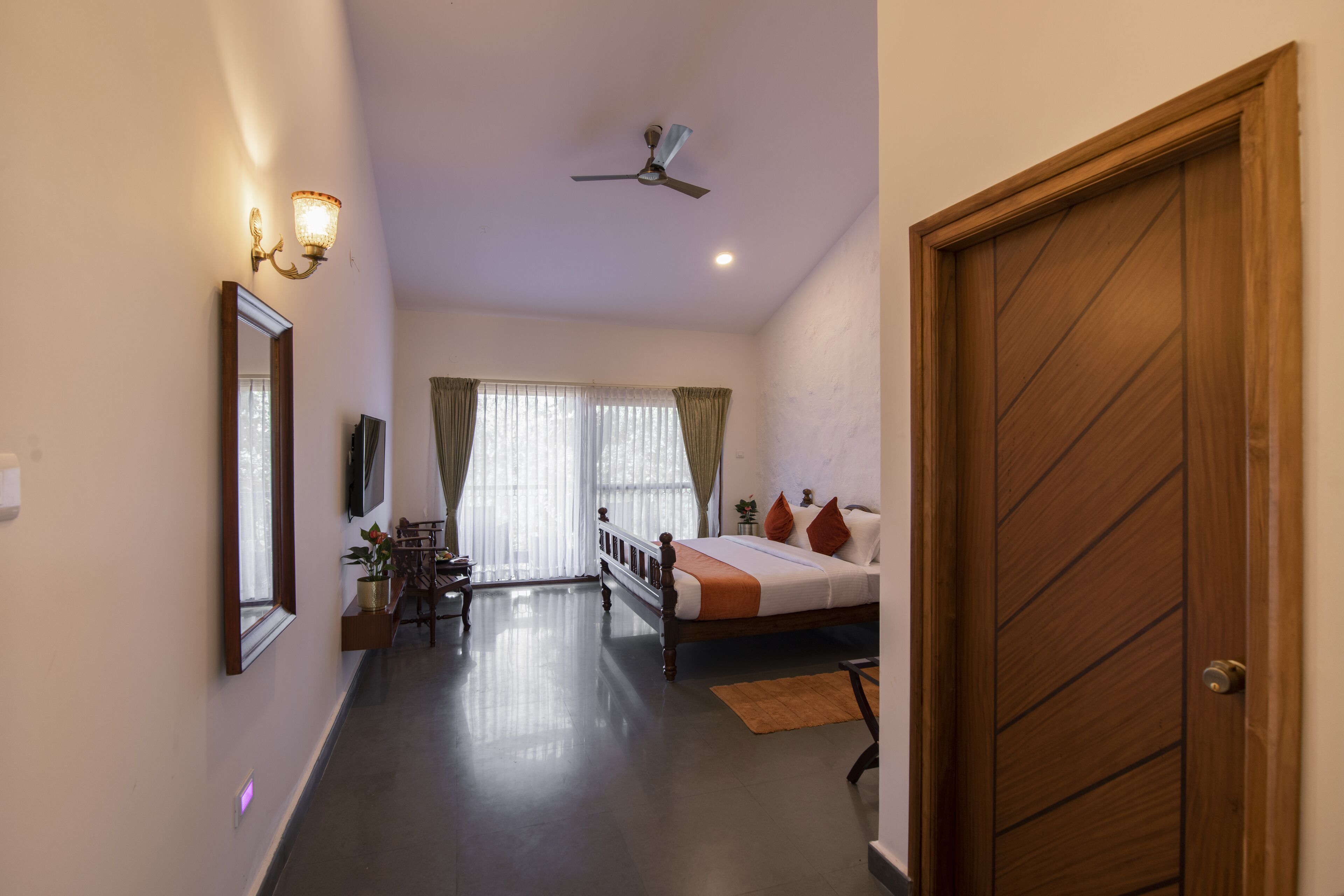 Una habitación de hotel con cama, escritorio, silla, ventilador de techo y puerta.