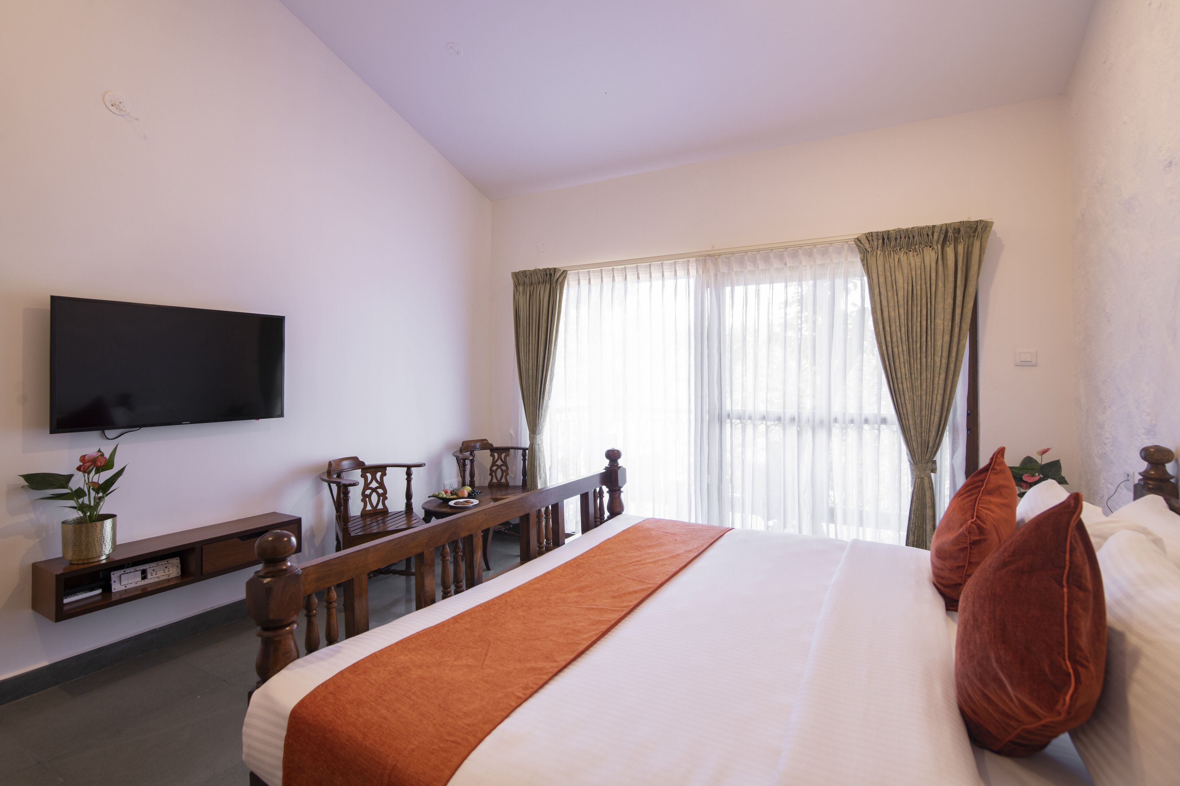 Camera d'albergo con un letto grande, una TV a schermo piatto fissata al muro, una panca di legno e una scrivania con una lampada.
