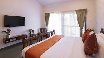 A hotel room with a large bed, a flat-screen TV mounted on the wall, a wooden bench, and a desk with a lamp.