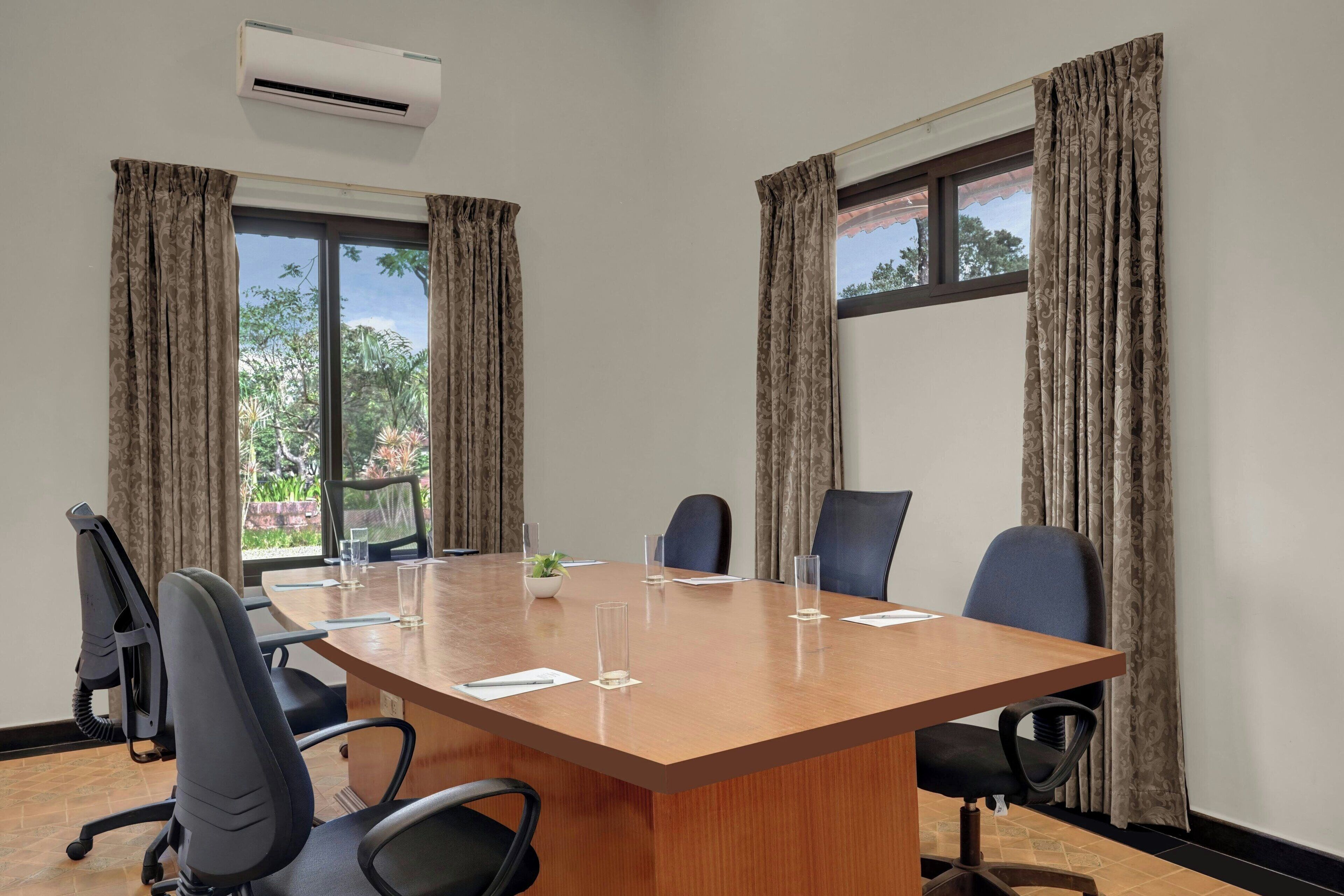 A conference room with a large wooden table, six black office chairs, and a potted plant.