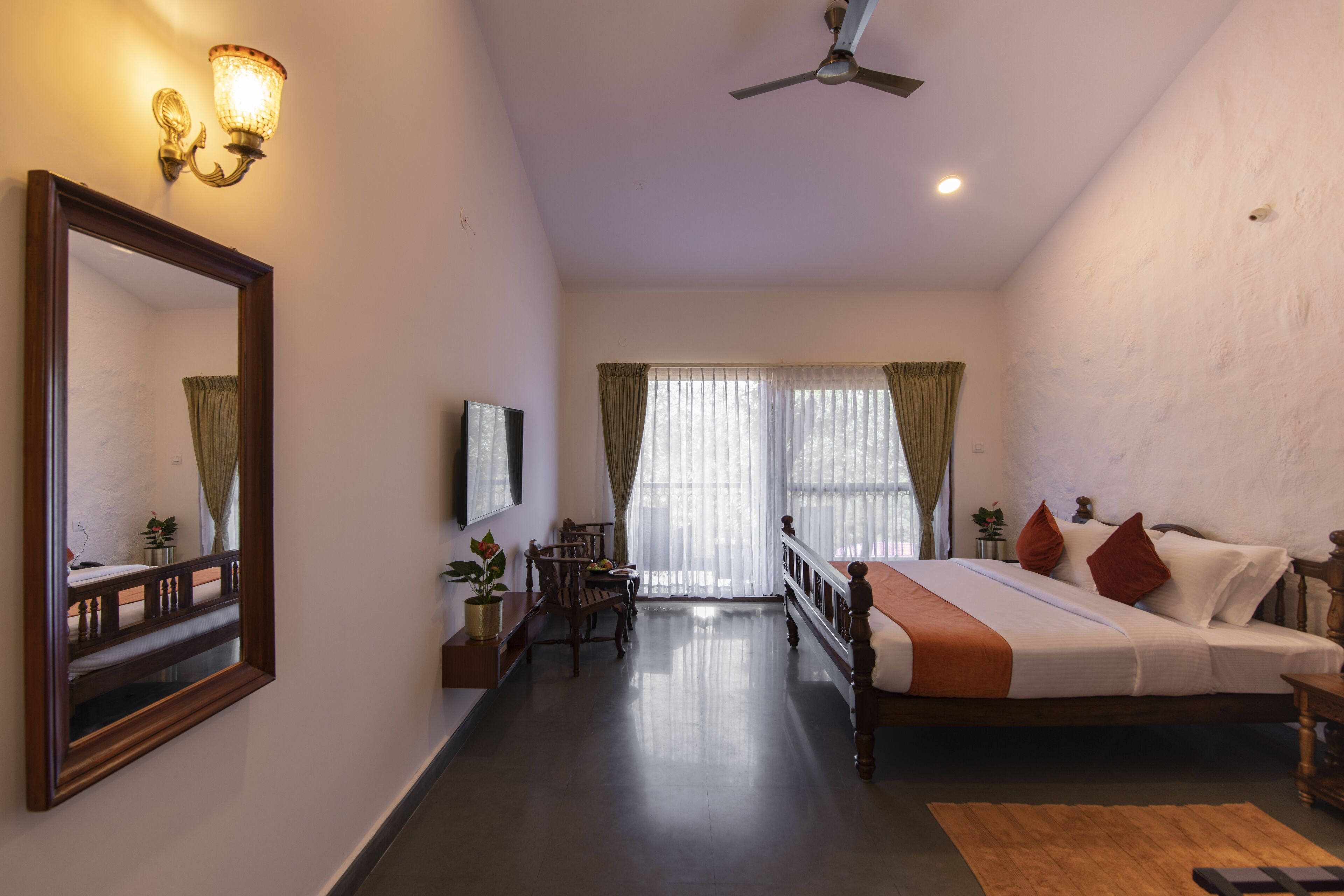 Une chambre d’hôtel équipée d’un lit, d’un bureau, d’une chaise, d’un miroir et d’un ventilateur de plafond.
