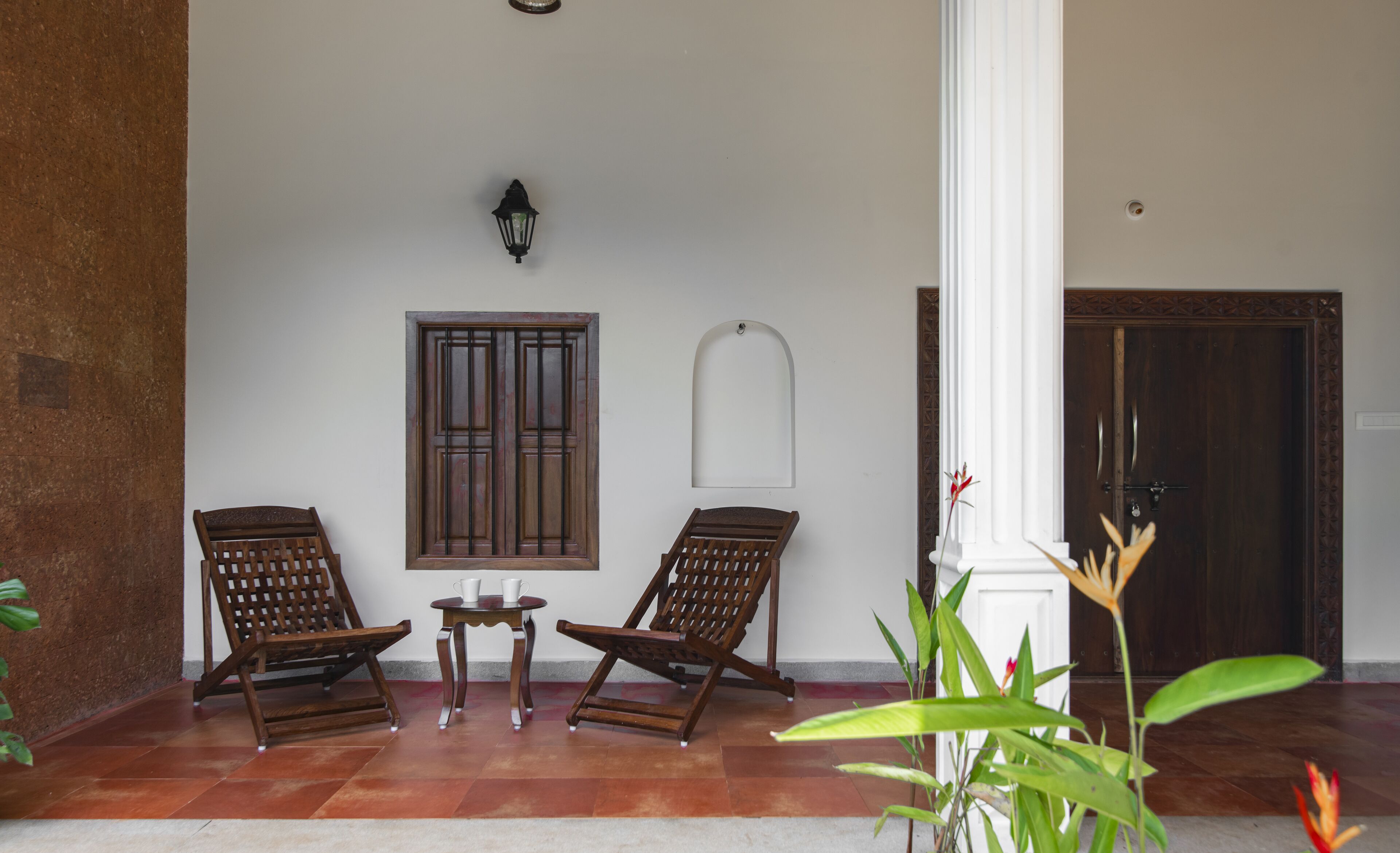A room with two wooden chairs, a small table, a wall-mounted light, and a door.