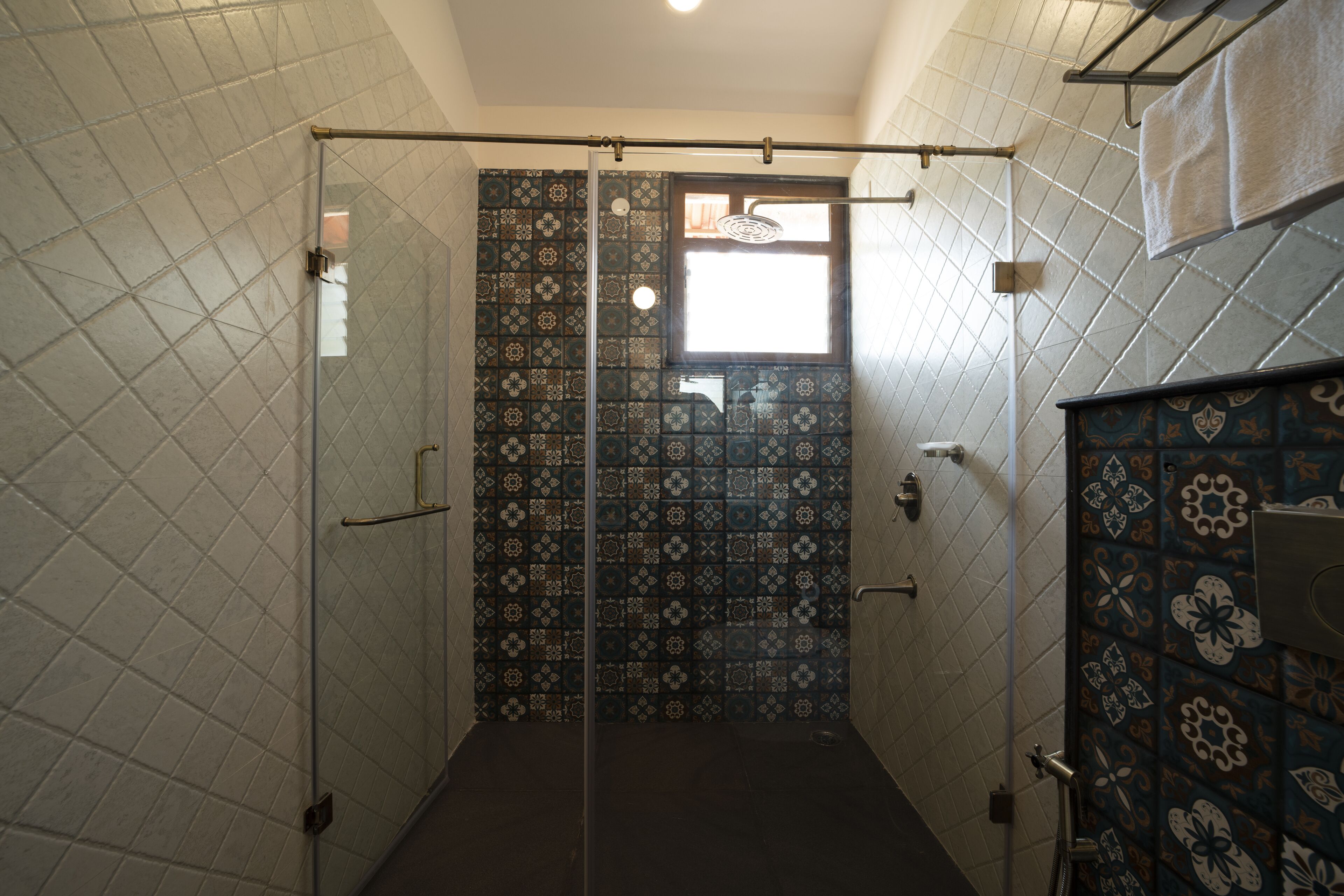 Un baño con baldosas estampadas, cabina de ducha de vidrio y un perchero para toallas.