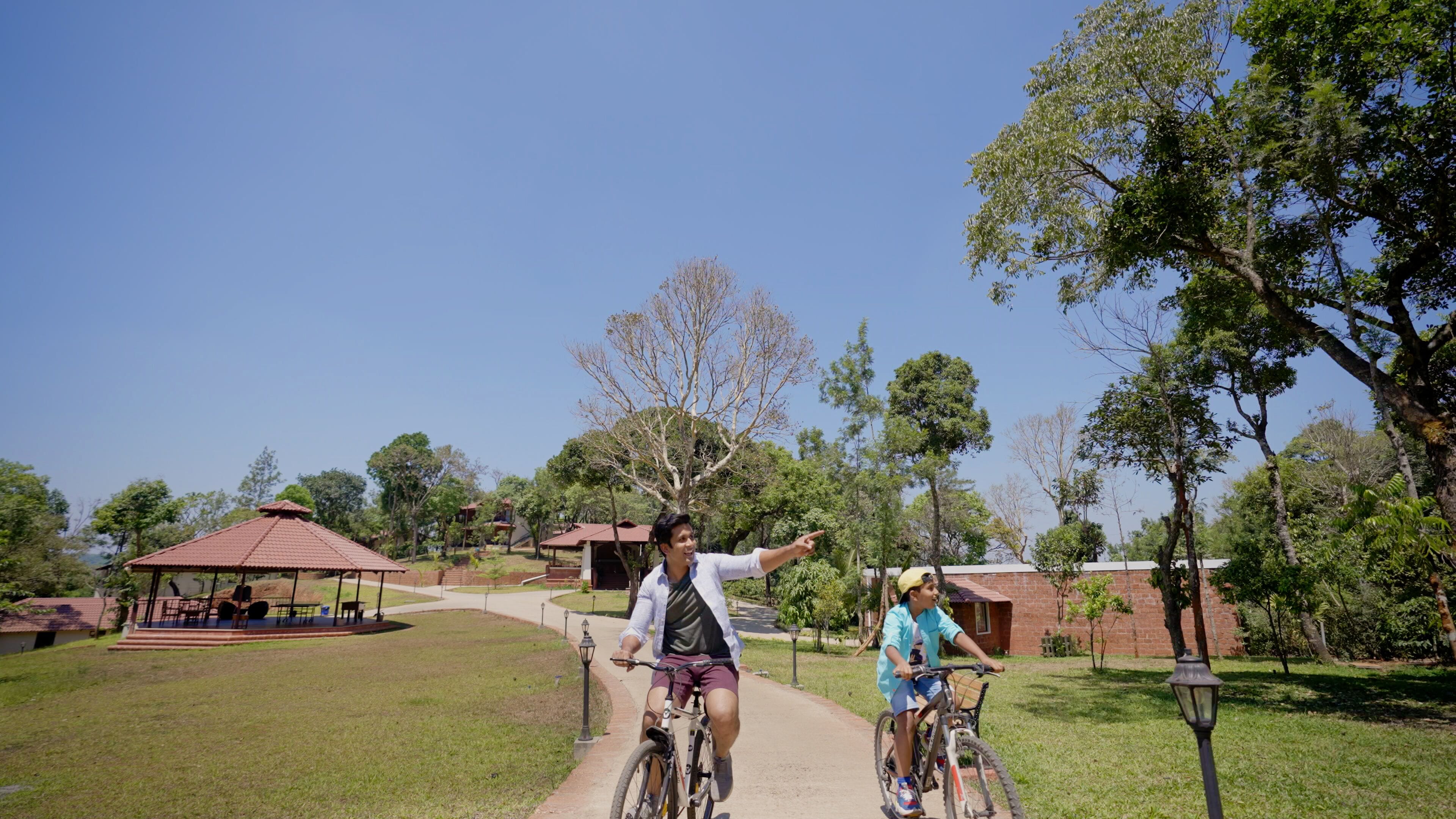 A pathway with two cyclists, a gazebo, and a brick building in a park.