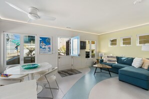 Un salon moderne avec un canapé bleu, une table basse blanche et un coin repas comprenant une table et des chaises blanches.