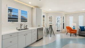 Een moderne keuken met witte kastjes, een ingebouwde vaatwasser en een eethoek met een tafel en stoelen.