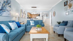 A spacious living room with a blue sofa set, a wooden coffee table, and a kitchen in the background. - Beach Paradise VIII-DOWNTOWN WATERFRONT 3BR Luxury Condo POOL-Beach-Boardwalk (Ocean City)